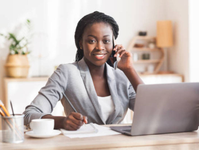 Portrait of black female entrepreneur talking on mobile phone, taking notes and smiling to camera